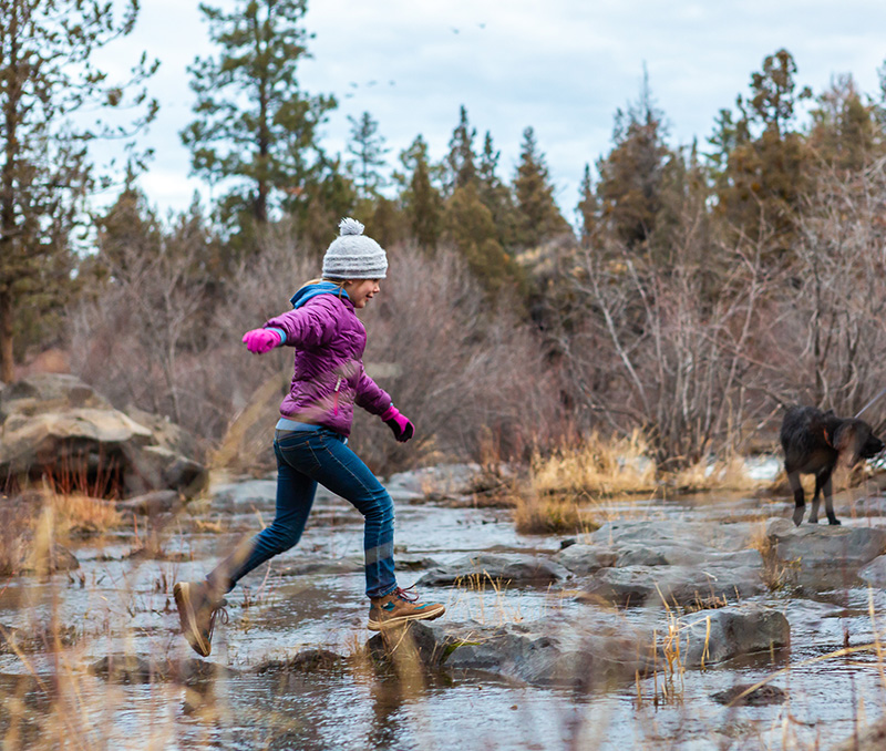 Girl jumping on stones across the Deschutes River in Bend, OR